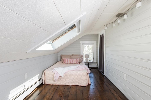 bedroom with wood walls, dark wood-style flooring, a baseboard heating unit, and vaulted ceiling with skylight