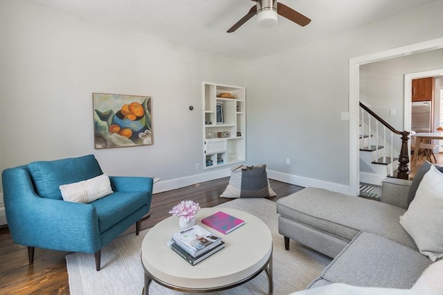 living room featuring a ceiling fan, baseboards, wood finished floors, and stairway