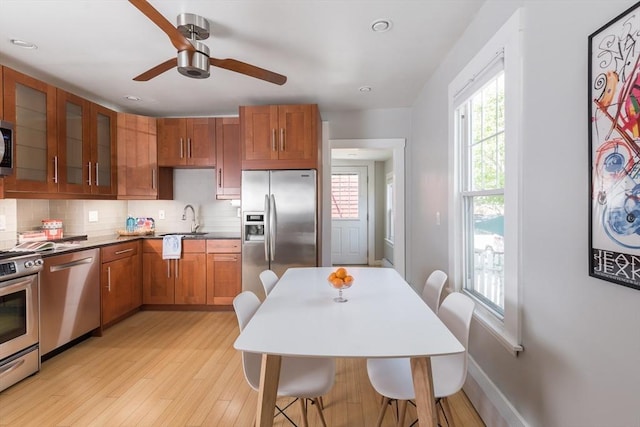 kitchen with glass insert cabinets, ceiling fan, backsplash, light wood-style floors, and stainless steel appliances