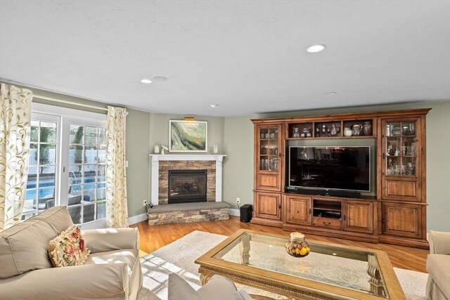 living area featuring baseboards, recessed lighting, a stone fireplace, and light wood-style flooring