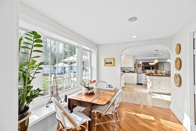 dining area featuring baseboards, arched walkways, light wood finished floors, and recessed lighting