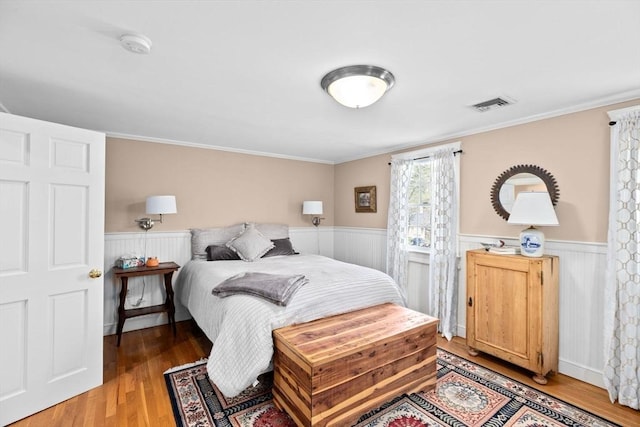 bedroom with wood finished floors, visible vents, ornamental molding, and wainscoting