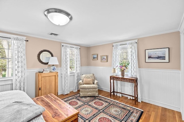 bedroom featuring wainscoting, wood finished floors, crown molding, and visible vents