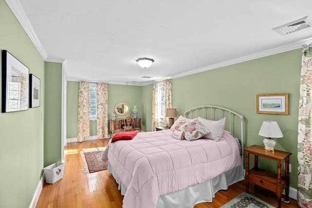 bedroom featuring wood finished floors, visible vents, crown molding, and baseboards