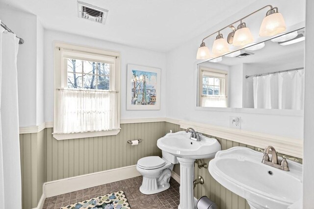 bathroom with a sink, a wainscoted wall, baseboards, toilet, and visible vents