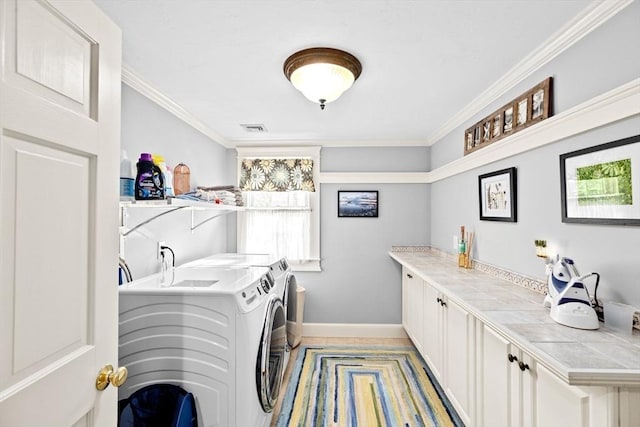 clothes washing area featuring washing machine and dryer, baseboards, ornamental molding, and cabinet space