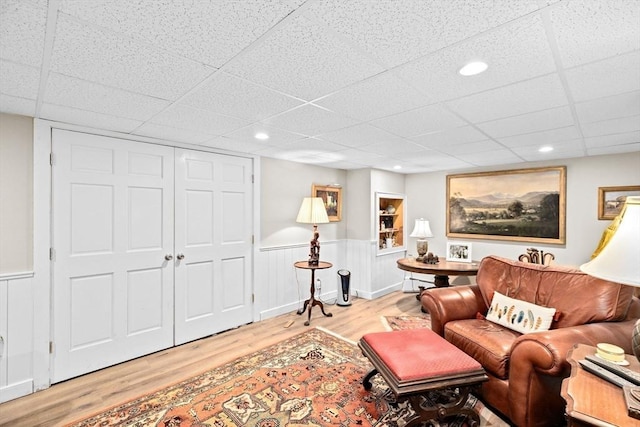 living room featuring wood finished floors, a drop ceiling, and wainscoting