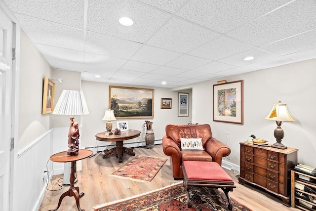 living area with a baseboard heating unit, a paneled ceiling, wood finished floors, and recessed lighting