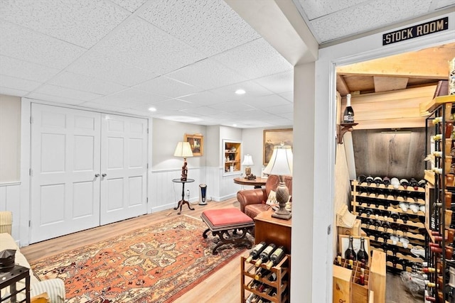 wine area featuring wainscoting, wood finished floors, and a drop ceiling