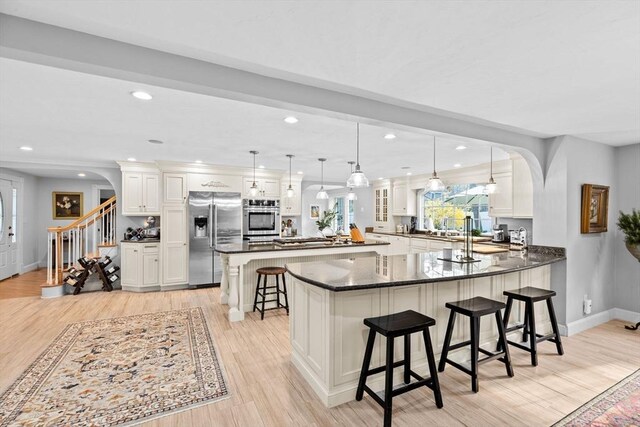 kitchen featuring a kitchen breakfast bar, stainless steel appliances, arched walkways, light wood-type flooring, and baseboards