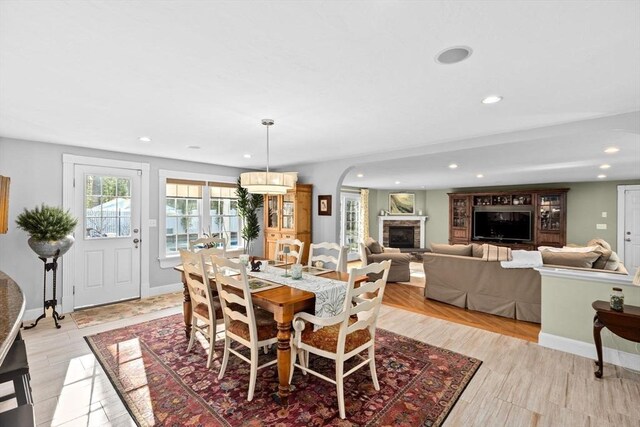 dining area featuring arched walkways, light wood-type flooring, baseboards, recessed lighting, and a stone fireplace