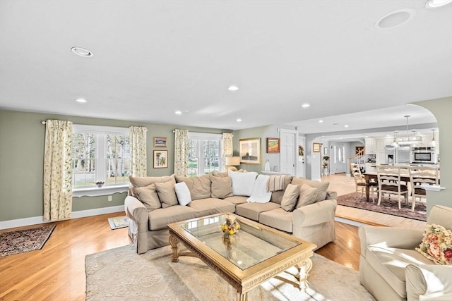 living area with recessed lighting, light wood-style flooring, arched walkways, and baseboards