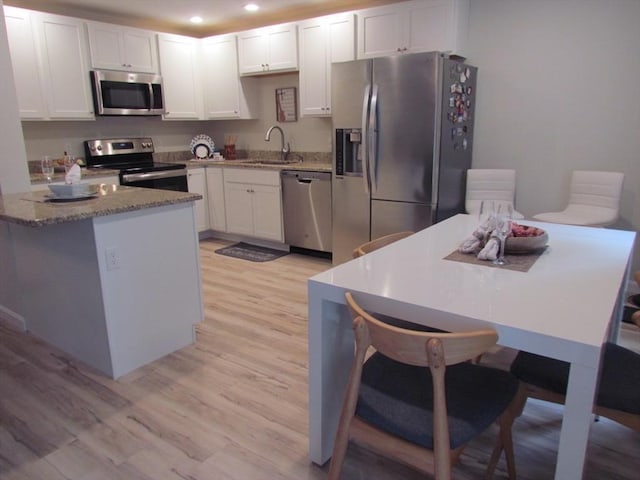 kitchen with white cabinetry, stainless steel appliances, light stone counters, and light hardwood / wood-style flooring