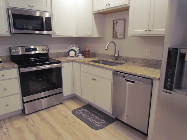 kitchen with appliances with stainless steel finishes, sink, white cabinets, light hardwood / wood-style floors, and light stone countertops