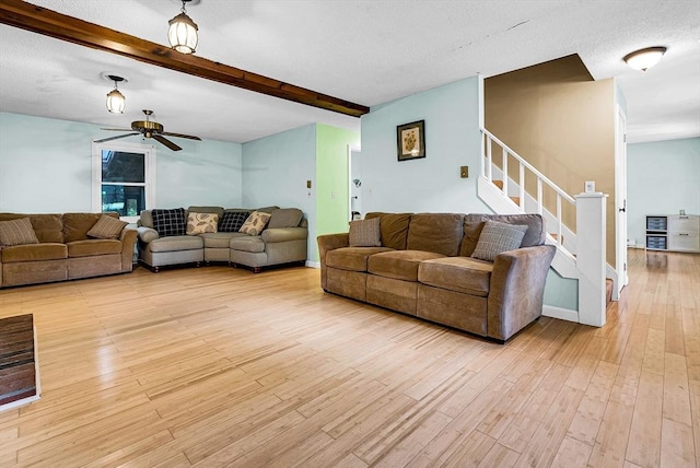 living area with a ceiling fan, stairs, a textured ceiling, light wood-type flooring, and beam ceiling