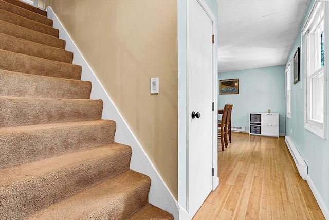 stairway with a baseboard radiator, baseboards, and wood finished floors