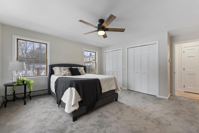 carpeted bedroom with a ceiling fan, baseboards, baseboard heating, and multiple closets