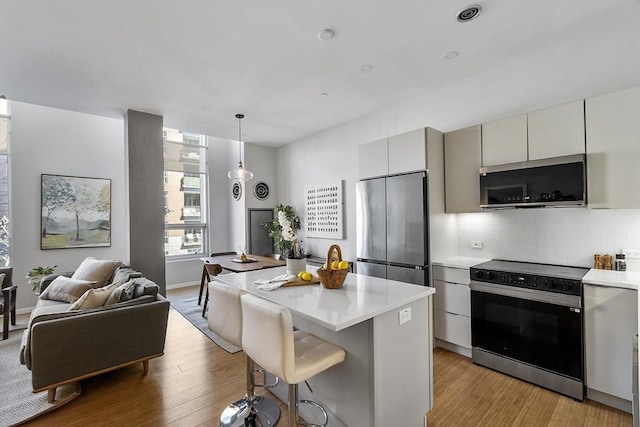kitchen featuring light countertops, appliances with stainless steel finishes, light wood-style floors, decorative backsplash, and a kitchen island