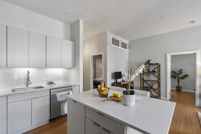 kitchen with tasteful backsplash, dishwasher, light countertops, a sink, and dark wood-style flooring
