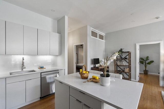 kitchen with dark wood finished floors, dishwasher, light countertops, a sink, and backsplash