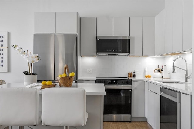 kitchen featuring modern cabinets, a sink, light countertops, stainless steel appliances, and backsplash