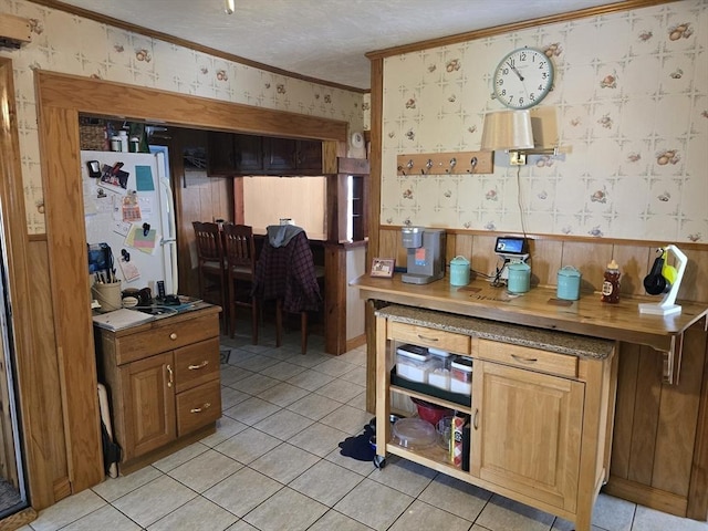 kitchen featuring freestanding refrigerator, light tile patterned flooring, wallpapered walls, and crown molding