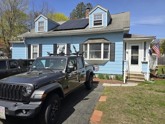 cape cod home featuring entry steps, a chimney, roof mounted solar panels, and roof with shingles