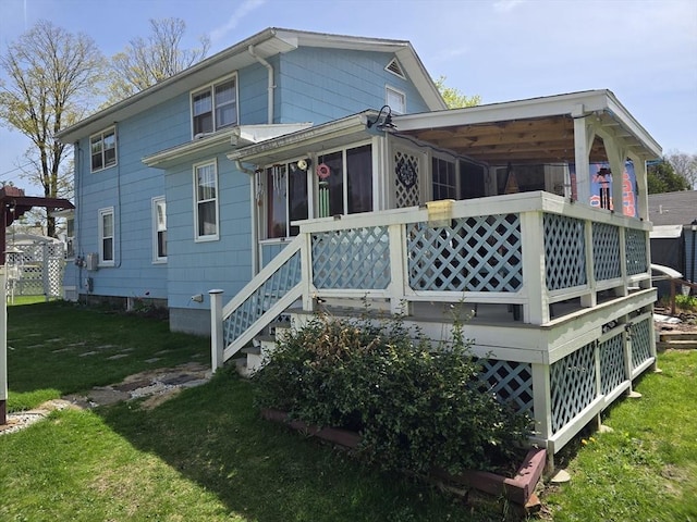 rear view of property featuring a lawn, a sunroom, and a deck