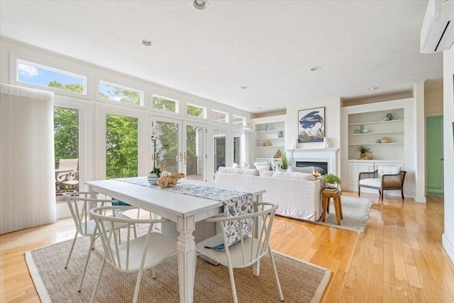 89 Standish Rd, Bourne, MA 02562 - dining area featuring a wall mounted air conditioner, light wood finished floors, a glass covered fireplace, built in shelves, and french doors