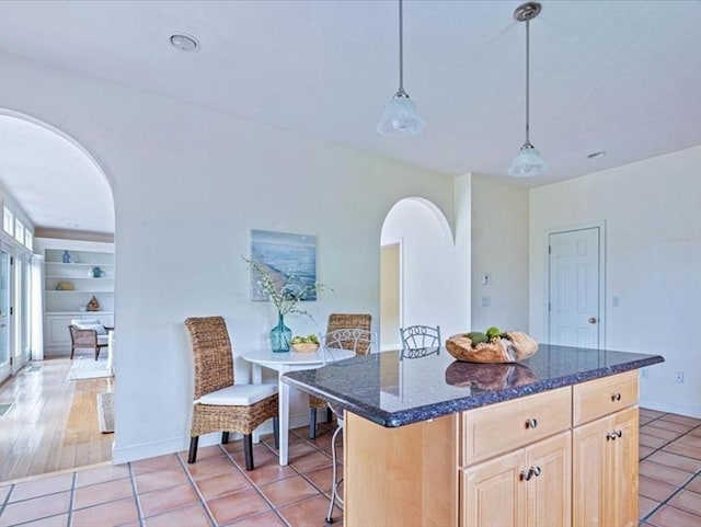 89 Standish Rd, Bourne, MA 02562 - kitchen featuring arched walkways, light brown cabinetry, dark stone counters, light tile patterned flooring, and a center island