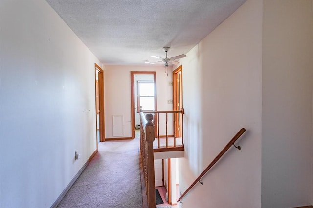 hallway featuring light carpet, baseboards, an upstairs landing, and a textured ceiling