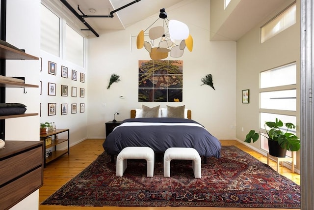 bedroom featuring a high ceiling, hardwood / wood-style flooring, and baseboards