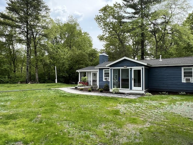 back of house featuring a lawn, a sunroom, a chimney, roof with shingles, and cooling unit