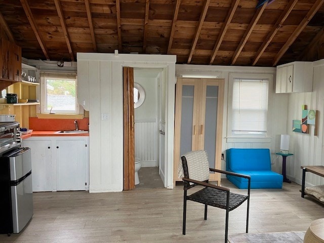 kitchen with white cabinets, sink, light wood-type flooring, and vaulted ceiling