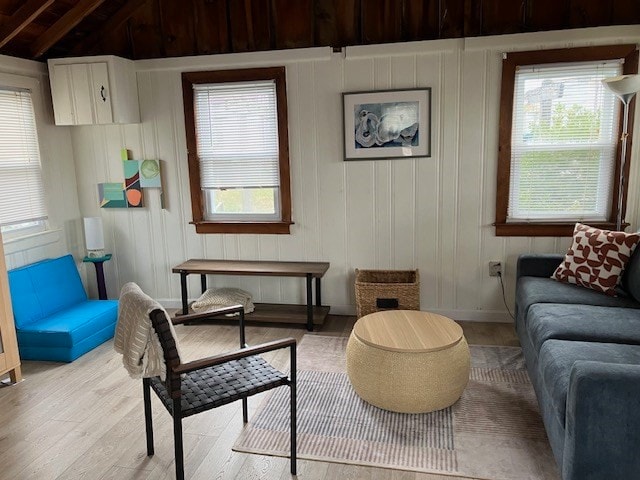 sitting room with lofted ceiling with beams, light wood-type flooring, and wood walls