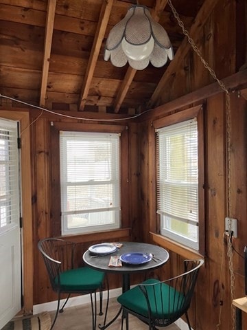 dining room with vaulted ceiling with beams, a healthy amount of sunlight, wooden walls, and wooden ceiling