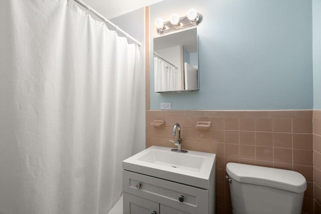 full bath featuring toilet, tile walls, wainscoting, and vanity