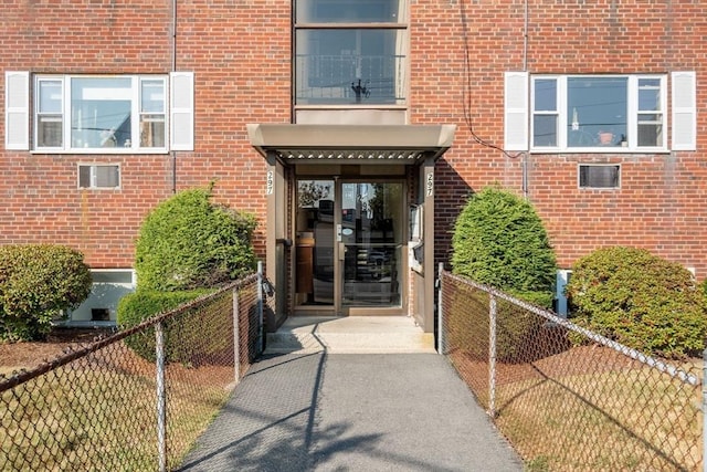 view of exterior entry with fence and brick siding