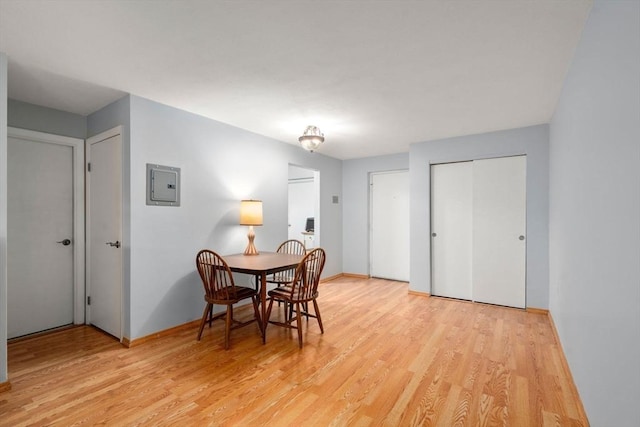 dining area with electric panel, baseboards, and light wood-style flooring