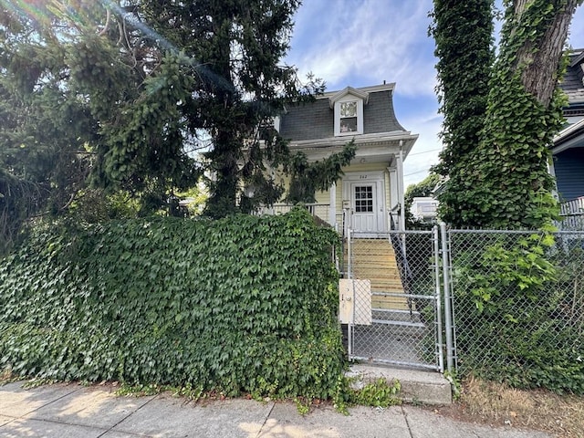 second empire-style home with a fenced front yard, a gate, mansard roof, and a shingled roof