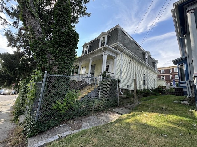 view of side of property featuring mansard roof, roof with shingles, covered porch, fence, and a yard