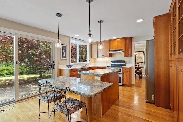 114 Hunters Ridge Rd, Concord, MA 01742 - kitchen featuring stainless steel appliances, a center island, brown cabinets, under cabinet range hood, and light wood-style floors