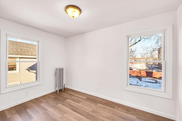 unfurnished room featuring a healthy amount of sunlight, radiator heating unit, and light hardwood / wood-style flooring