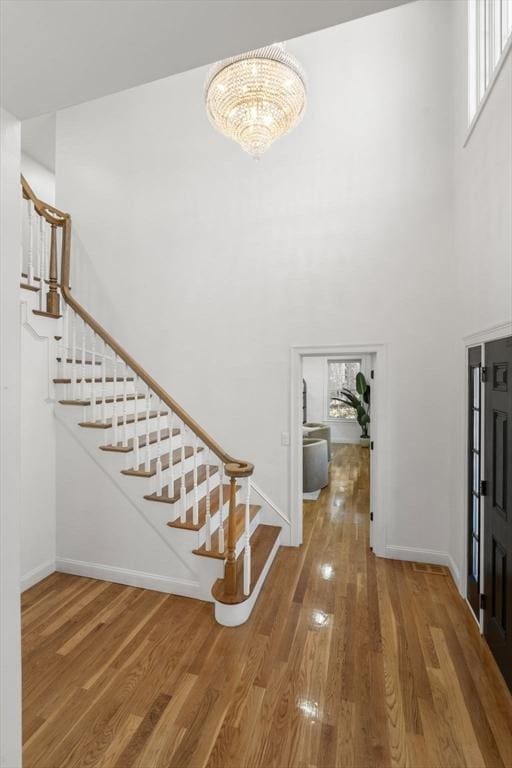 foyer entrance with a notable chandelier, wood finished floors, a towering ceiling, baseboards, and stairs