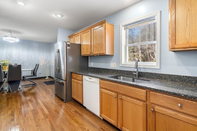 kitchen featuring dishwasher, light wood-type flooring, stainless steel fridge, sink, and dark stone countertops