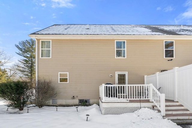 snow covered back of property with a deck