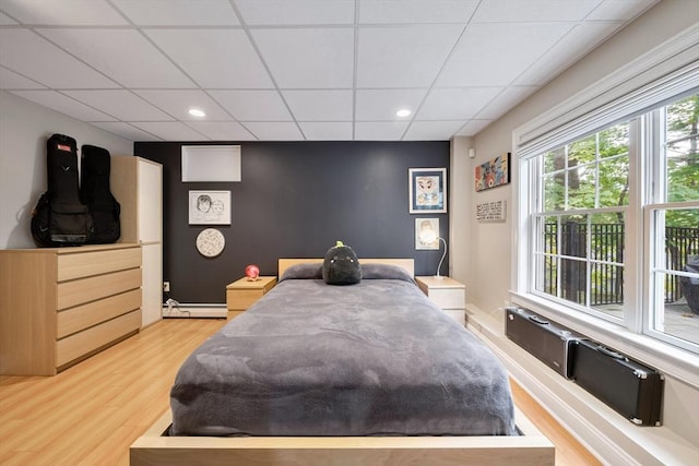 bedroom with a drop ceiling, a baseboard radiator, and light hardwood / wood-style flooring