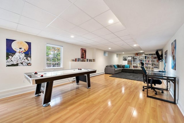 recreation room featuring baseboard heating, hardwood / wood-style floors, and a drop ceiling