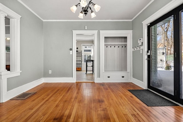 interior space with a chandelier, light wood-style flooring, visible vents, baseboards, and ornamental molding