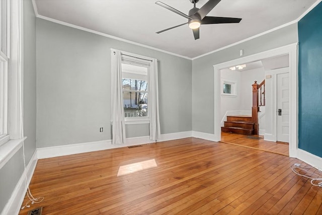 empty room with stairs, hardwood / wood-style floors, crown molding, and baseboards